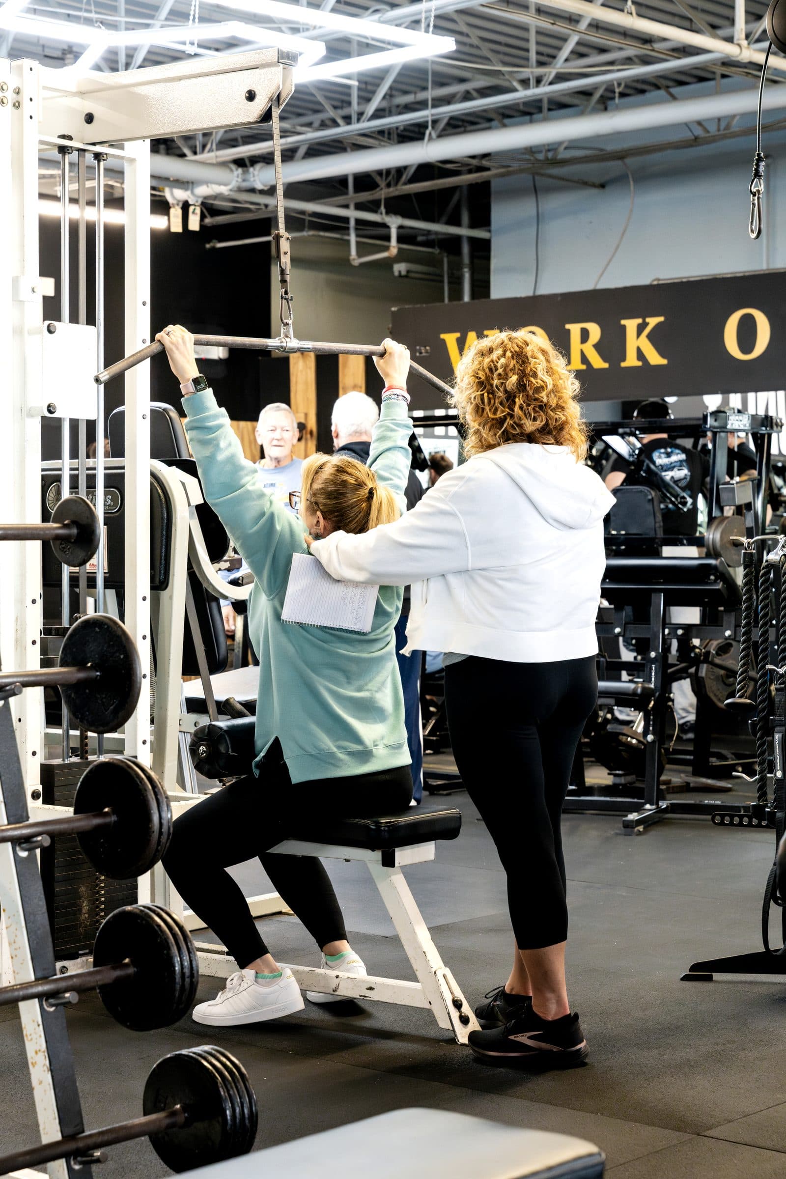 A coach guides a member through a lat pulldown while other members train nearby at an existing W.O.L.F. Gyms location (source photo Brig14-Requested.jpg).