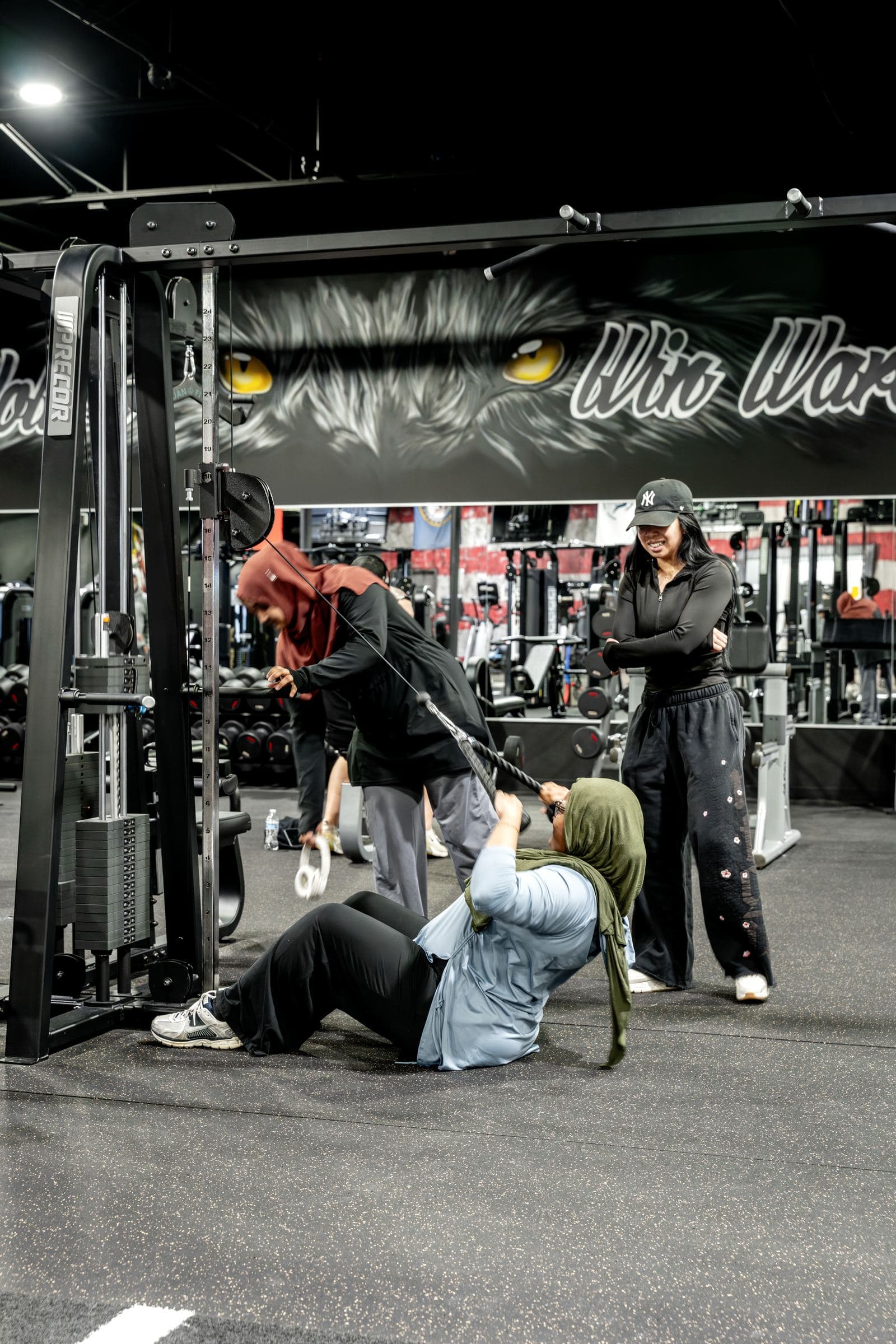 Members train together on a cable machine beneath a painted wolf-eyes mural at an existing W.O.L.F. Gyms location (source photo Wolf-Gyms11-Requested.jpg).